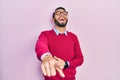 Hispanic man with beard wearing business shirt and glasses laughing at you, pointing finger to the camera with hand over body, Royalty Free Stock Photo