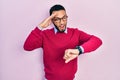 Hispanic man with beard wearing business shirt and glasses looking at the watch time worried, afraid of getting late Royalty Free Stock Photo