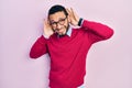Hispanic man with beard wearing business shirt and glasses trying to hear both hands on ear gesture, curious for gossip Royalty Free Stock Photo