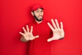 Hispanic man with beard wearing delivery uniform and cap afraid and terrified with fear expression stop gesture with hands, Royalty Free Stock Photo