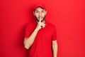 Hispanic man with beard wearing delivery uniform and cap asking to be quiet with finger on lips