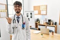Hispanic man with beard wearing doctor uniform and stethoscope at the office smiling with happy face looking and pointing to the Royalty Free Stock Photo