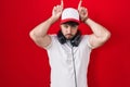 Hispanic man with beard wearing gamer hat and headphones doing funny gesture with finger over head as bull horns