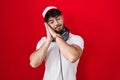 Hispanic man with beard wearing gamer hat and headphones sleeping tired dreaming and posing with hands together while smiling with Royalty Free Stock Photo