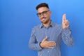 Hispanic man with beard wearing glasses smiling swearing with hand on chest and fingers up, making a loyalty promise oath Royalty Free Stock Photo