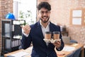 Hispanic man with beard working at the office holding coffee pointing thumb up to the side smiling happy with open mouth Royalty Free Stock Photo