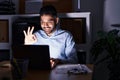 Hispanic man with beard working at the office with laptop at night doing ok sign with fingers, smiling friendly gesturing Royalty Free Stock Photo