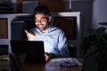 Hispanic man with beard working at the office with laptop at night pointing thumb up to the side smiling happy with open mouth Royalty Free Stock Photo