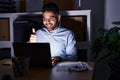 Hispanic man with beard working at the office with laptop at night smiling happy and positive, thumb up doing excellent and Royalty Free Stock Photo