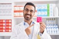 Hispanic man with beard working at pharmacy drugstore holding condom smiling happy pointing with hand and finger Royalty Free Stock Photo