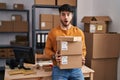 Hispanic man with beard working at small business ecommerce holding packages afraid and shocked with surprise and amazed Royalty Free Stock Photo