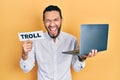 Hispanic man with beard working using computer laptop holding banner with troll word smiling and laughing hard out loud because Royalty Free Stock Photo