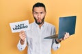 Hispanic man with beard working using computer laptop holding lazy loading banner making fish face with mouth and squinting eyes,