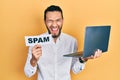 Hispanic man with beard working using computer laptop holding spam banner smiling and laughing hard out loud because funny crazy Royalty Free Stock Photo