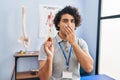 Hispanic man with curly hair holding cbd oil covering mouth with hand, shocked and afraid for mistake Royalty Free Stock Photo