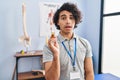 Hispanic man with curly hair holding cbd oil scared and amazed with open mouth for surprise, disbelief face Royalty Free Stock Photo