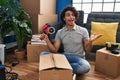 Hispanic man with curly hair moving to a new home closing cardboard box with tape celebrating achievement with happy smile and Royalty Free Stock Photo