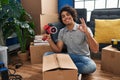 Hispanic man with curly hair moving to a new home closing cardboard box with tape doing ok sign with fingers, smiling friendly Royalty Free Stock Photo