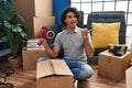 Hispanic man with curly hair moving to a new home closing cardboard box with tape pointing thumb up to the side smiling happy with Royalty Free Stock Photo