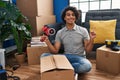 Hispanic man with curly hair moving to a new home closing cardboard box with tape smiling happy pointing with hand and finger to Royalty Free Stock Photo