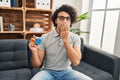 Hispanic man with curly hair playing colorful puzzle cube intelligence game covering mouth with hand, shocked and afraid for