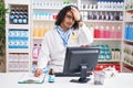 Hispanic man with curly hair working at pharmacy drugstore surprised with hand on head for mistake, remember error