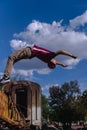 Hispanic man dressed in red with urban clothing doing a somersault with an abandoned train and the sky in the background. Latin