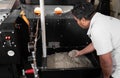 An Hispanic man is dropping coffee beans in a roaster machine.