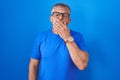 Hispanic man with grey hair standing over blue background bored yawning tired covering mouth with hand Royalty Free Stock Photo