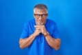 Hispanic man with grey hair standing over blue background laughing nervous and excited with hands on chin looking to the side Royalty Free Stock Photo