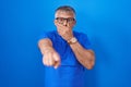 Hispanic man with grey hair standing over blue background laughing at you, pointing finger to the camera with hand over mouth, Royalty Free Stock Photo