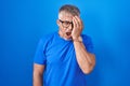 Hispanic man with grey hair standing over blue background yawning tired covering half face, eye and mouth with hand Royalty Free Stock Photo