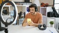 Hispanic man with headphones in studio using smartphone, music equipment backdrop Royalty Free Stock Photo
