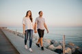 A Hispanic man and his girlfriend are strolling on a breakwater in Spain