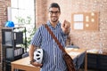 Hispanic man with long hair working at the office holding bike helmet pointing to you and the camera with fingers, smiling Royalty Free Stock Photo