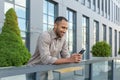 hispanic man outside modern office building using smartphone, businessman in shirt typing message and browsing online Royalty Free Stock Photo