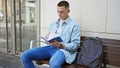 A hispanic man reads a book on a university campus bench, backpack beside him, radiating youth and studiousness Royalty Free Stock Photo