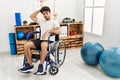 Hispanic man sitting on wheelchair at physiotherapy clinic confuse and wonder about question Royalty Free Stock Photo