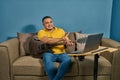 Hispanic man on a sofa in front of his laptop Greeting fellow students in the online guitar class