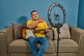 Hispanic man on a sofa in front of his tablet Greeting fellow students in the online guitar class