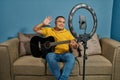 Hispanic man on a sofa in front of his tablet Greeting fellow students in the online guitar class