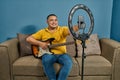 Hispanic man on a sofa in front of his tablet Greeting fellow students in the online guitar class
