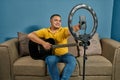 Hispanic man on a sofa in front of his tablet Greeting fellow students in the online guitar class