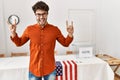 Hispanic man standing by election room shouting with crazy expression doing rock symbol with hands up