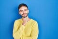 Hispanic man standing over blue background with hand on chin thinking about question, pensive expression Royalty Free Stock Photo