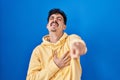 Hispanic man standing over blue background laughing at you, pointing finger to the camera with hand over body, shame expression Royalty Free Stock Photo