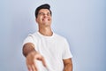 Hispanic man standing over blue background laughing at you, pointing finger to the camera with hand over body, shame expression Royalty Free Stock Photo