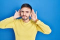 Hispanic man standing over blue background trying to hear both hands on ear gesture, curious for gossip Royalty Free Stock Photo