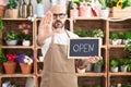Hispanic man with tattoos working at florist holding open sign with open hand doing stop sign with serious and confident