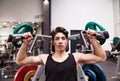 Hispanic man training in gym, doing machine shoulder press.